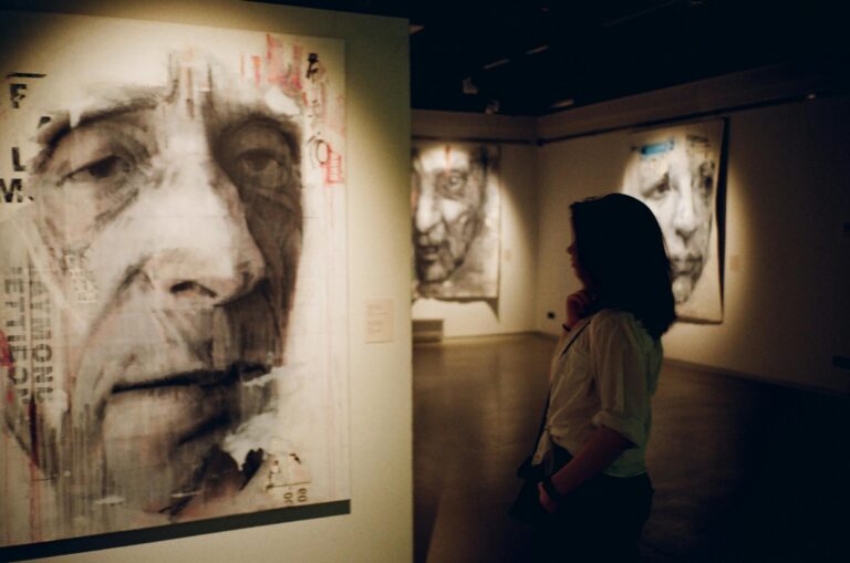 A woman observes portrait paintings in a dimly lit modern art gallery.