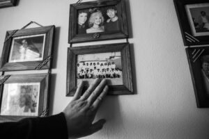 A hand touching vintage black and white framed family photos on a wall, evoking nostalgia.