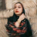 Blurred artistic portrait of a woman in a black hijab against a textured stone wall.