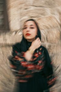 Blurred artistic portrait of a woman in a black hijab against a textured stone wall.