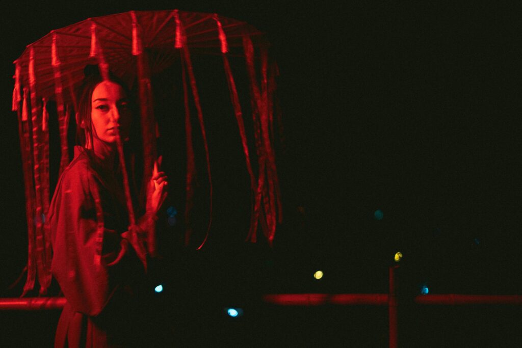 Artistic portrait of a woman in a kimono under an umbrella, highlighted by red light.